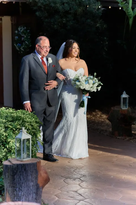 Bride walks through the garden with her escort and white bouquet.