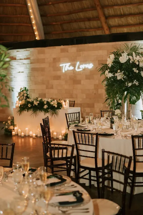 Candlelit sweetheart table sits against a warm stone reception wall.