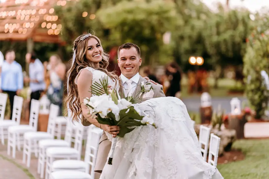 Newlyweds smiling between rows of white ceremony chairs at Longan’s Place