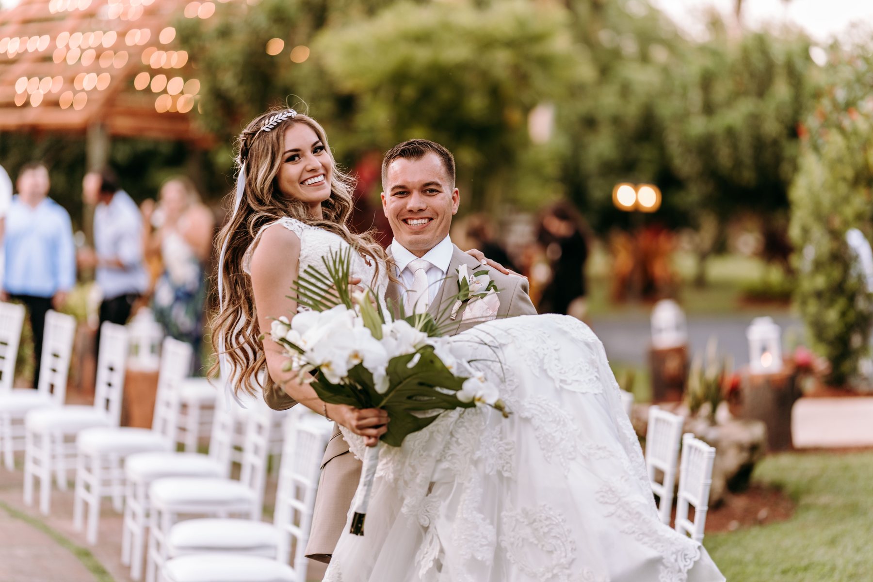 Newlyweds smiling between rows of white ceremony chairs at Longan’s Place