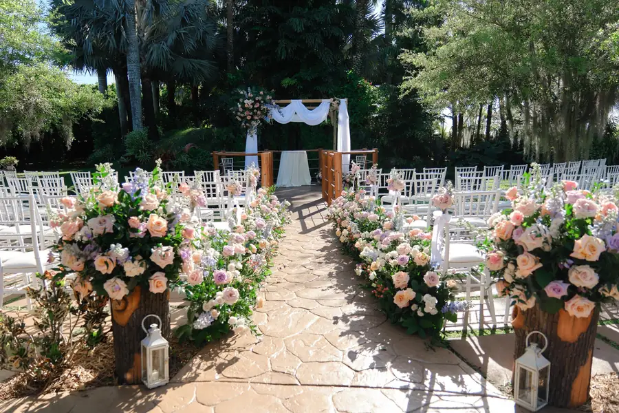 Flower-lined garden wedding aisle with white chairs beside the pond at Longan’s Place in Miami’s Redland