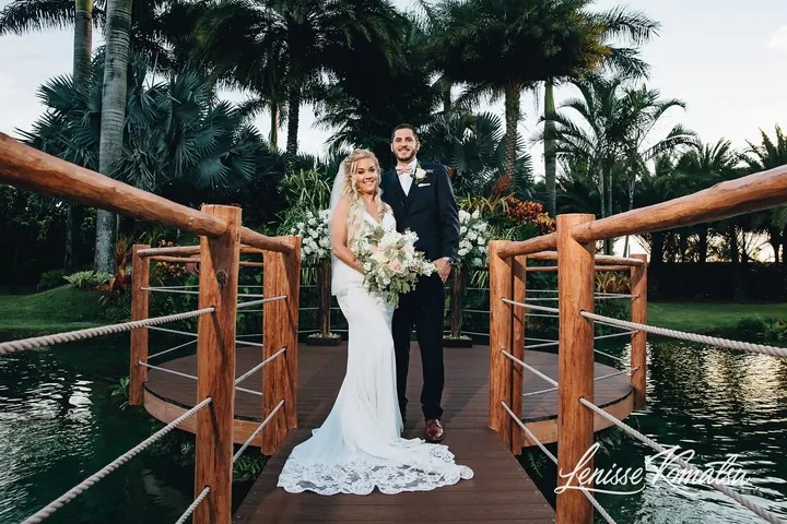Newlyweds walk together across the wooden bridge over the pond.