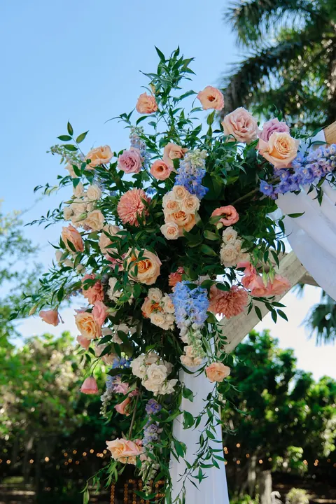 Pastel roses and blue flowers decorate a garden ceremony arch.