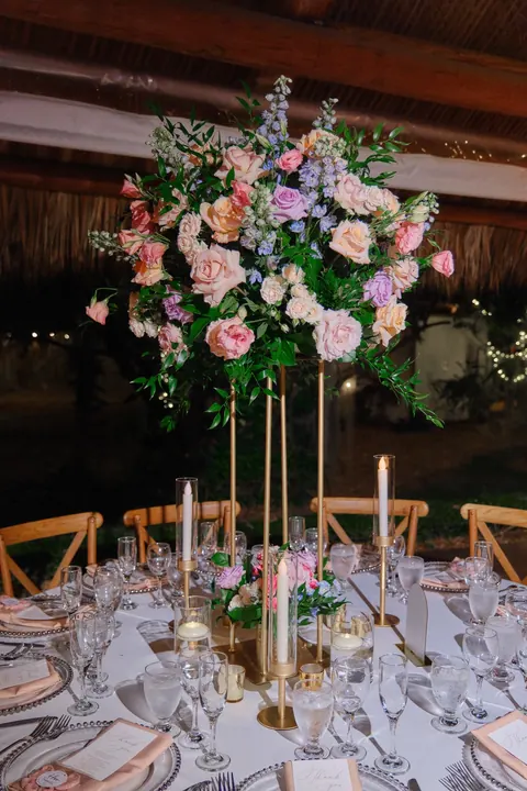 Pastel roses and greenery form a tall gold reception centerpiece.