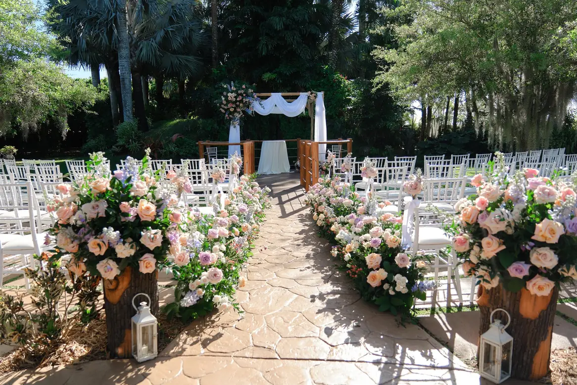 Flower lined garden ceremony aisle at Longan’s Place with white guest chairs and tropical trees