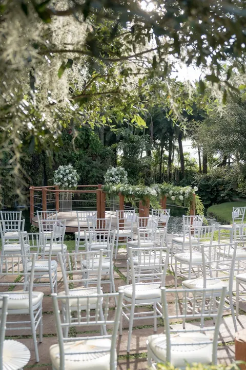White chairs face a flower decorated wooden bridge beside the pond.